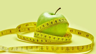 Sarı bir arka plan üzerinde bir ölçüm bandı ile izole yeşil elma