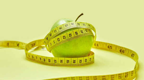 Isolated green apple with a measuring tape on a yellow background