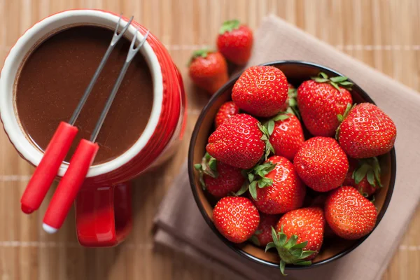 Sobremesa. fondue de chocolate em uma xícara vermelha com morangos maduros e brilhantes em um fundo de madeira — Fotografia de Stock