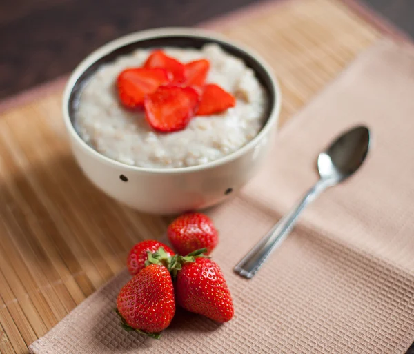 Harina de avena caliente, con trozos de fresas y cacao caliente con leche sobre una mesa de madera — Foto de Stock