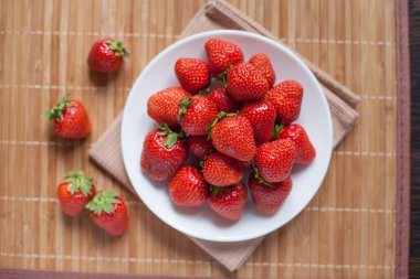 ahşap arka plan üzerinde beyaz bir tabak içinde parlak, olgun, lezzetli çilek