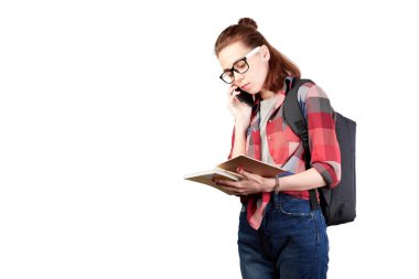 Genç öğrenci, telefonda, beyaz arka planda izole edilmiş. Sırt çantasında not defterine yazı yazan sıradan bir kız öğrenci portresi beyaz arka planda izole edilmiş kitaplarla dikiliyordu.