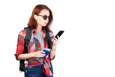 Yürüyen ve beyaz arka planda izole edilmiş bir cep telefonuna bakan bir bayan yürüyüşçü. Yürüyüş. Sırt çantası, pasaportu ve uçak biletleri olan bir kız..