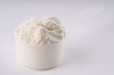 Beyaz zemin üzerinde protein tozu yığını. Protein tozu Scoops 'u. Kaşığı ve vanilya protein tozunu ölçüyorum..