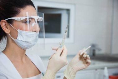 Kadın stomatolog, elinde neşterle diş ameliyatına hazır..