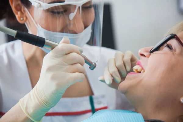 Smiling patient on chair and dentist with drill.