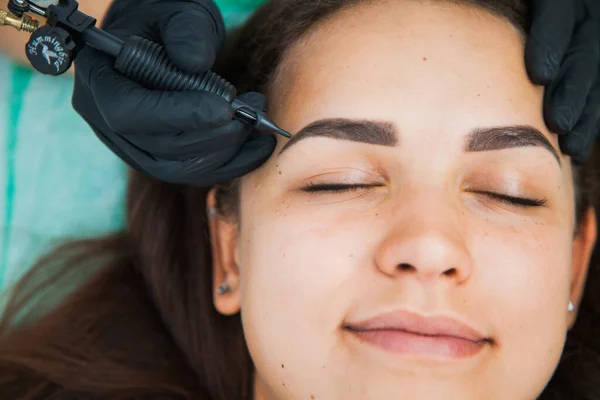 Young woman on permanent make-up procedure, tattooing eyebrows