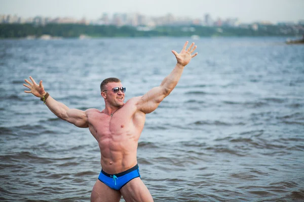 Snygg atletisk kille med glada ansikte och händer upp, känna frihet vid floden. — Stockfoto