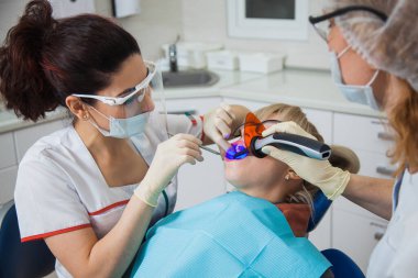 Diş hekimi ve koruma maskeli asistanın diş boşluğuyla çalışırken yakın plan fotoğrafı..