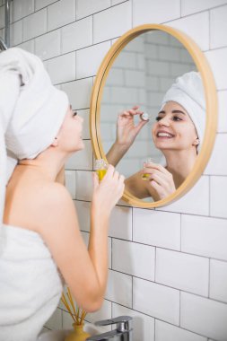 Beyaz havluyla genç bir kadın cildine nemlendirici yağ sürüyor..