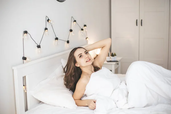 Красивая молодая женщина просыпается в удобной постели на белых свежих простынях. — стоковое фото