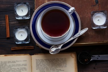 Eski kitap, çay mumlar, gümüş kaşık, çay yaprakları ve koyu ahşap zemin üzerine tarçın çay kompozisyonu.