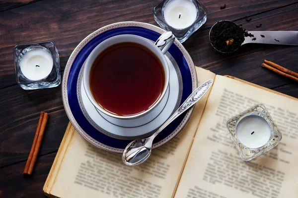 Teekomposition mit altem Buch, Teekerzen, Silberlöffel, Teeblättern und Zimt auf dunklem Holzgrund. — Stockfoto