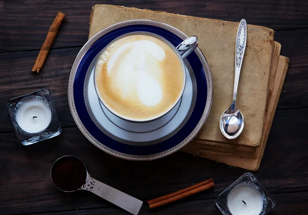 Kaffeekomposition mit altem Buch, weißen Teelichtern, Silberlöffel, gemahlenem Kaffee und Zimt auf dunklem Holzgrund. — Stockfoto