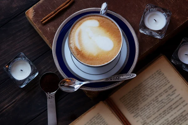 Kaffeekomposition mit altem Buch, weißen Teelichtern, Silberlöffel, gemahlenem Kaffee und Zimt auf dunklem Holzgrund. — Stockfoto