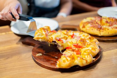 Restoranda yanında spatulayla peynirli pizza servis eden birine yakın çekim. Eritilmiş peynir ve malzemelerle kaplı taze pişmiş pizza. Yemek, yemek ve İtalyan mutfağı kavramları için ideal..