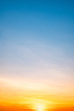 Sunset or sunrise sky with a vibrant gradient of orange, gold, and soft blue. Clear atmosphere with wispy clouds. Peaceful, natural light background. hope, freedom, new day Concepts, Vertical