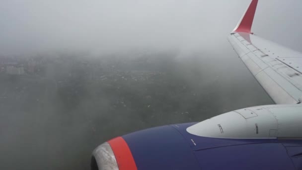 Widok turbiny i skrzydła z okna samolotu. Samolot jest bardzo nisko nad ziemią. Niska chmura. Białe chmury mijają. Samolot ląduje. — Wideo stockowe