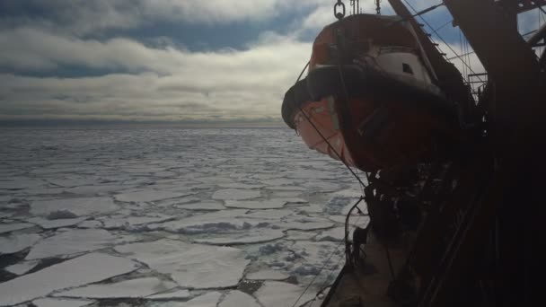 Vista de um barco de resgate em um navio que navega através do gelo. O navio navega através do gelo. Barco de resgate laranja em um navio grande. Volta para estibordo. Pedaços de gelo no mar. O quebra-gelo — Vídeo de Stock