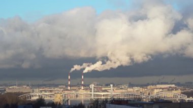 Şehrin üzerindeki bir termik santralin borularından çıkan beyaz duman. Bacalardan çıkan duman bulutlarla birleşir. Megalopolis. Nehir köprüsü. Mavi gökyüzünde beyaz duman. Duman bulutlara karışıyor.