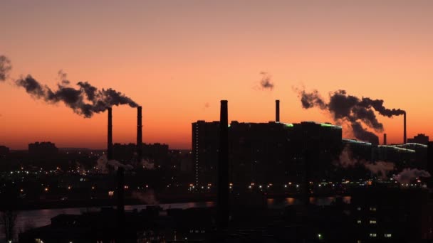 Fumo de canos na cidade contra o céu vermelho. Tubos e casas em silhueta. Há muitos canos à volta de edifícios residenciais. De manhã cedo. — Vídeo de Stock