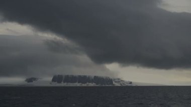 Karla kaplı kayaların üzerinde kara bir bulut. Soğuk denizin kıyısındaki yüksek uçurumlar.