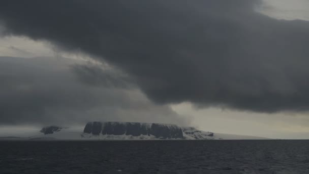 Uma nuvem escura sobre as rochas cobertas de neve. Falésias altas na costa do mar frio. — Vídeo de Stock