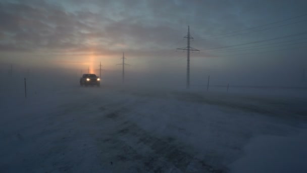 Автомобілі з фарами, що їздять у сильну сніжну бурю. Автомобіль їде по дорозі сильним вітром. Зима. Сніг обривається по дорозі . — стокове відео