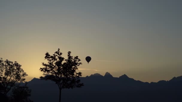 The balloon takes off over the line of mountains. A silhouette. The general plan. A small tree in the foreground. — Stock Video