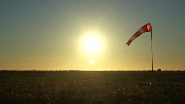 Windsock na modré obloze. Rudá a bílá ponožka ve větru. Slunce svítí do objektivu. Malé letadlo na obloze v pozadí — Stock video