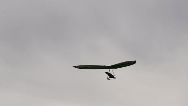 Le deltaplane vole. Une silhouette. L'aile et le pilote en dessous. Ciel gris sur le fond. — Video