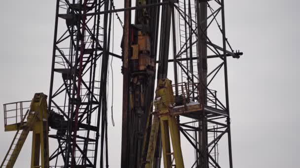 Drilling rig. The drill is spinning. Drilling rig. The drill is spinning. Top drive goes down. Metal tower. Yellow supports. Metal supports against the sky — Wideo stockowe