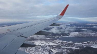 The wing of plane. View from the eluminator. Clouds fly by below. Winter. Lilac, blue snow. Beautiful landscape. River, forest, villages