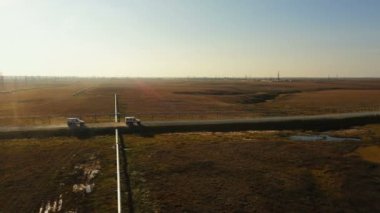 Cars drive on road in tundra. Clouds of dust behind All-terrain vehicles. Aerial view. A drilling rig in the background. Cross-country vehicles