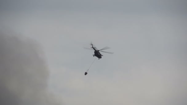 Helicopter flies with a bambi bucket. Military helicopter. Silhouette in the sky. — Stock video