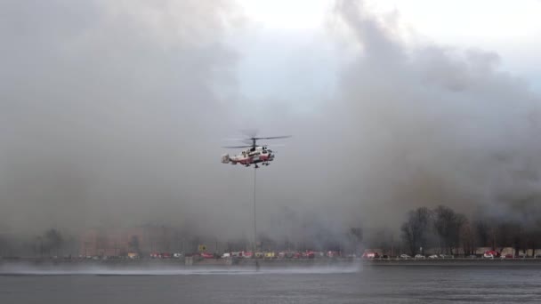 Helikoptern plockar upp bambi hinken från floden. Räddningshelikopter svävade. Brandhelikopter lågt över floden. KA-32. Rök bakom — Stockvideo