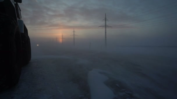 Вантажівка йде в снігопаді. Сильний вітер. Снігова буря. Вихідне сонце. Силові полюси. Снігопад. Лоррі їде на крижаній дорозі. Автомобіль їде під сильним снігопадом — стокове відео