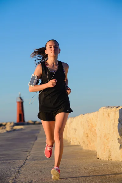 Joven chica deportiva corriendo sola en la hermosa puesta de sol cerca del faro . — Foto de Stock