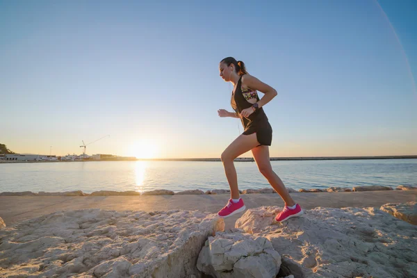 Joven chica deportiva corriendo sola en la hermosa puesta de sol en la playa — Foto de Stock