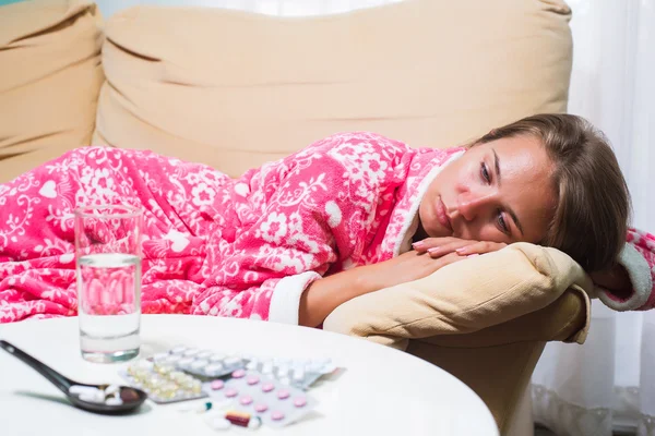 Mujer enferma acostada en la cama en bata mirando el termómetro y las pastillas — Foto de Stock