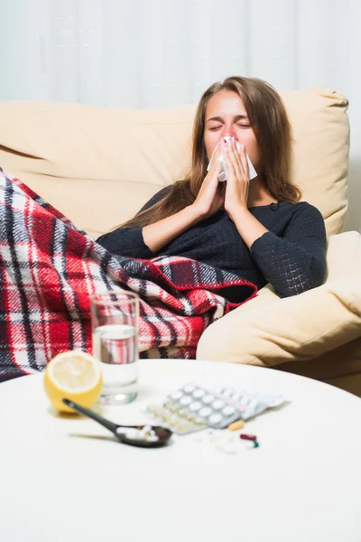 Zieke vrouw liggend op de Bank onder wollen deken niezen en vegen neus — Stockfoto