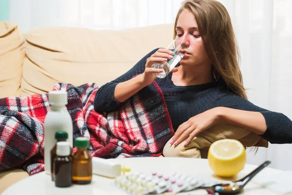 Sick woman lying on sofa under wool blanket drinking water — Stock Photo, Image