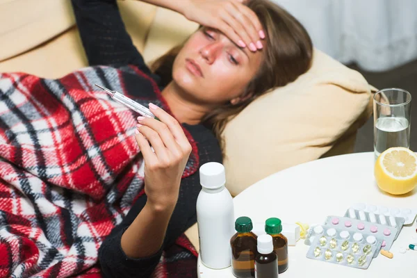 Zieke vrouw liggend op de Bank onder wollen deken en kijken naar thermometer — Stockfoto