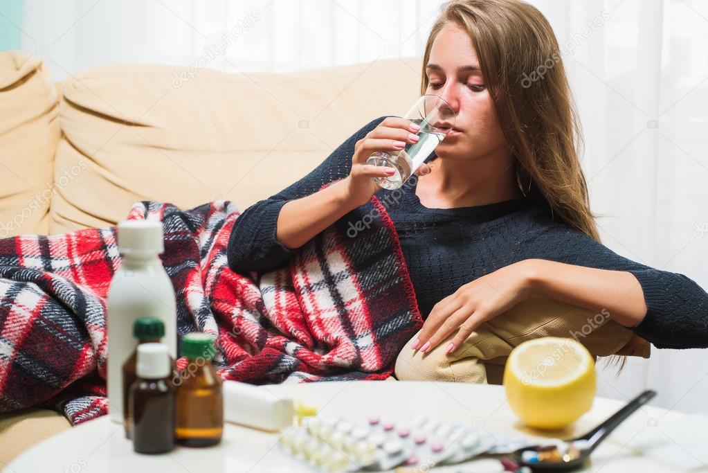 Sick woman lying on sofa under wool blanket drinking water