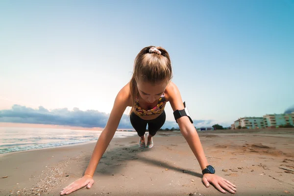Linda chica en forma haciendo ejercicio de tablón en la playa al amanecer — Foto de Stock