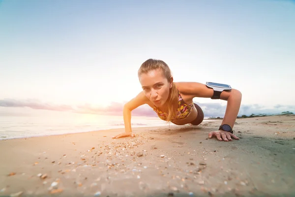 Joven chica deportiva haciendo flexiones en la playa al amanecer — Foto de Stock