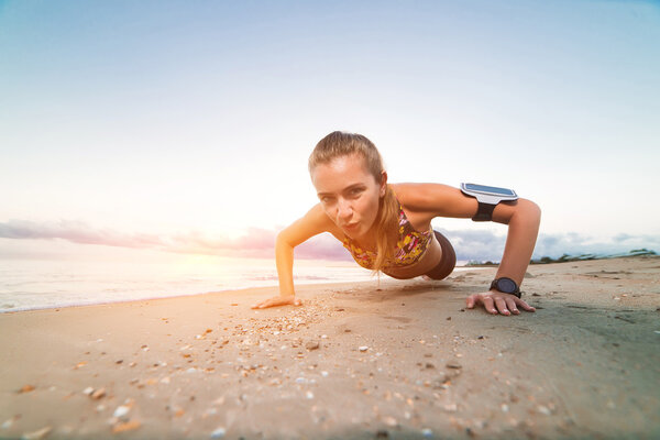 Young sporty girl doing push ups on beach at sunrise