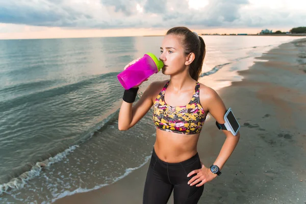 Chica en forma joven beber agua en la playa después del entrenamiento de la mañana — Foto de Stock