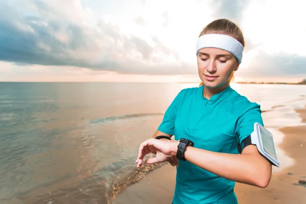 Joven chica deportiva mirando el reloj en la playa amanecer — Foto de Stock