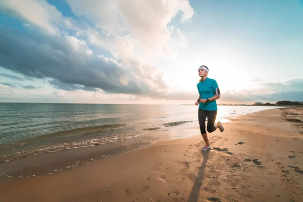 Joven chica deportiva corriendo en la playa al amanecer en la mañana — Foto de Stock